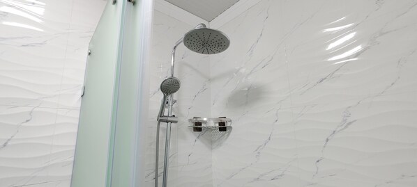 Doccia con soffione a mano e soffione a parete in un bagno dalle pareti in marmo.