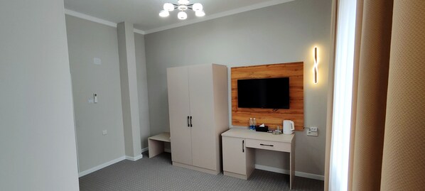 A bedroom with a bed, a wardrobe, a desk, and a television mounted on the wall. - Cozy Hotel (Bishkek)