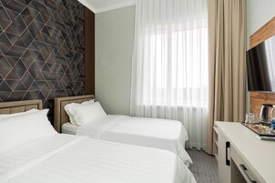 Habitación de hotel con dos camas, cabecero de madera, un amplio ventanal con cortinas translúcidas, un escritorio de madera y un televisor de pantalla plana.