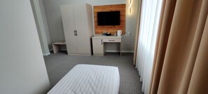 A hotel room with a bed, a desk, a wardrobe, and a television mounted on the wall. - Cozy Hotel (Bishkek)