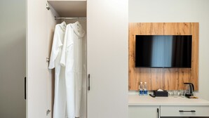 Une salle de bain moderne équipée d’une douche, d’un peignoir blanc, d’un mur recouvert de panneaux en bois, d’un téléviseur à écran plat et d’un petit bureau avec une machine à café.