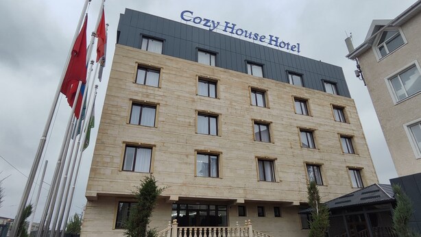 Un immeuble à plusieurs étages, sur lequel on peut lire l’inscription « Cozy House Hotel » au sommet.
