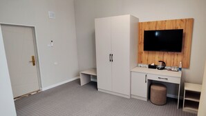 Une chambre d’hôtel équipée d’une kitchenette, d’un téléviseur fixé sur un panneau en bois, d’une porte et d’un petit tabouret.