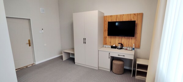 Ein Hotelzimmer mit Küchenzeile, einem an einer Holzplatte montierten Fernseher, einer Tür und einem kleinen Hocker.