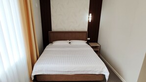 Une chambre d’hôtel avec un lit simple, une table de chevet et une fenêtre avec des stores.