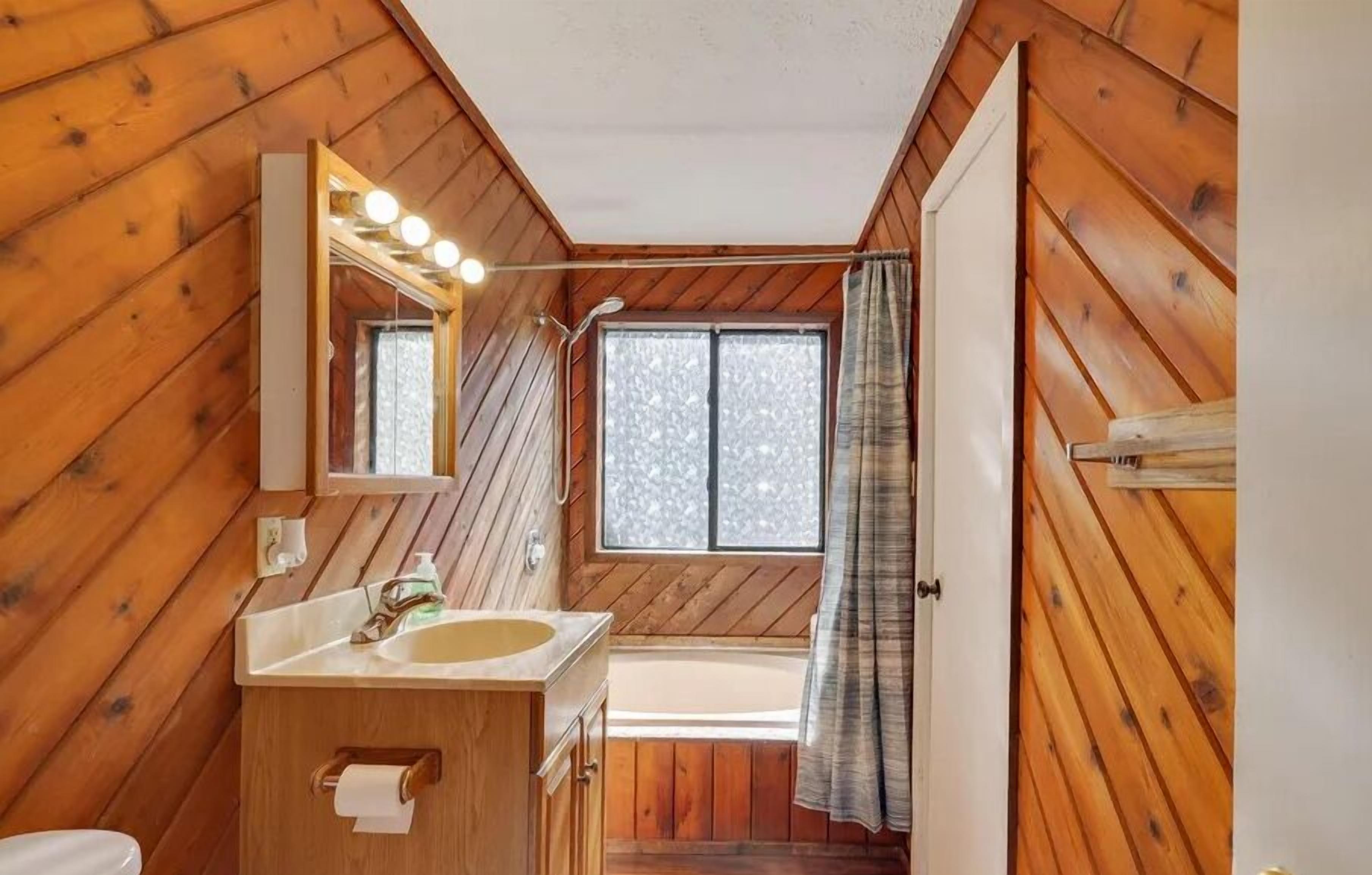 A wooden cabin bathroom with a sink, mirror, and window.