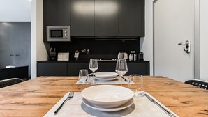 Una mesa de comedor preparada con platos, vasos y cubiertos en una cocina moderna con armarios oscuros y un microondas.