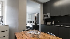 Una cocina moderna con armarios oscuros, un microondas y una zona de comedor con una mesa de madera y dos tazas.