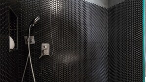 Un baño con pared de diseño tipo panal de abeja, un cabezal de ducha y un panel de control.