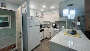 Una cocina compacta con armarios blancos, microondas integrado, estufa a gas y refrigerador.