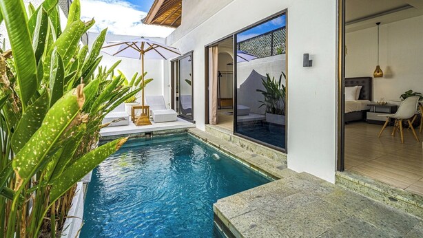 A modern outdoor pool area with a clear view of the pool, a seating area with a table and chairs, and a large window offering a view of the interior.