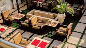 A restaurant with multiple tables and chairs, a large potted plant, and a tiled floor. - Tchetche Hotel & Restaurant (Accra)