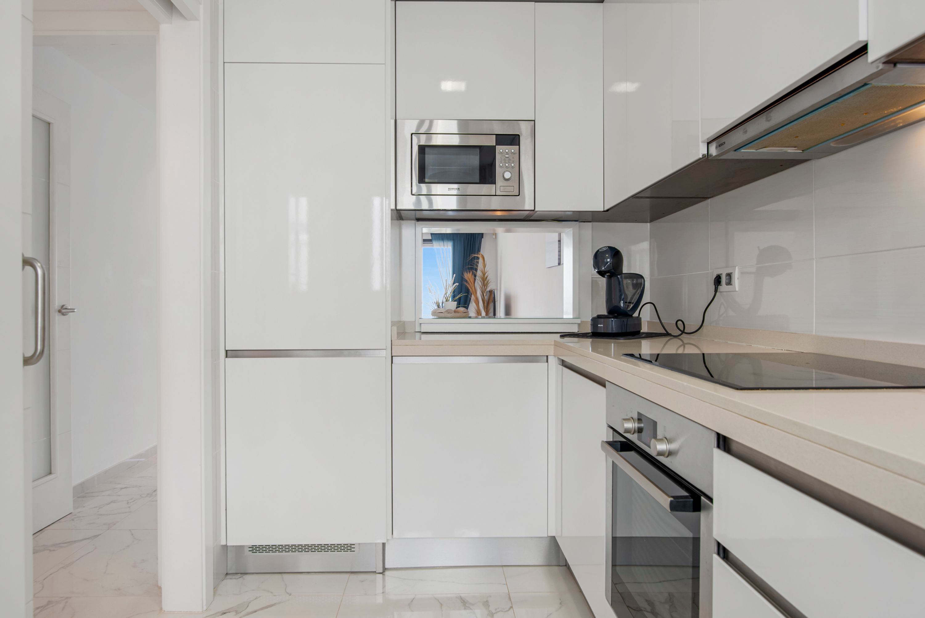 A modern kitchen with white cabinetry, a built-in microwave, a coffee maker, and a stove.