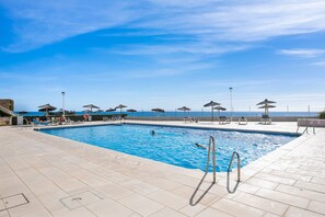 Ein Schwimmbecken mit Blick auf das Meer, Liegestühle und Sonnenschirme.