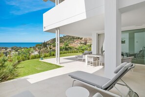 Een modern terras buiten met een lounge stoel, een tafel en een glazen ruimte met zitplaatsen.
