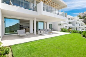 Een modern huis met twee verdiepingen, een ruime patio, een eethoek en een keuken zichtbaar door grote glazen deuren.