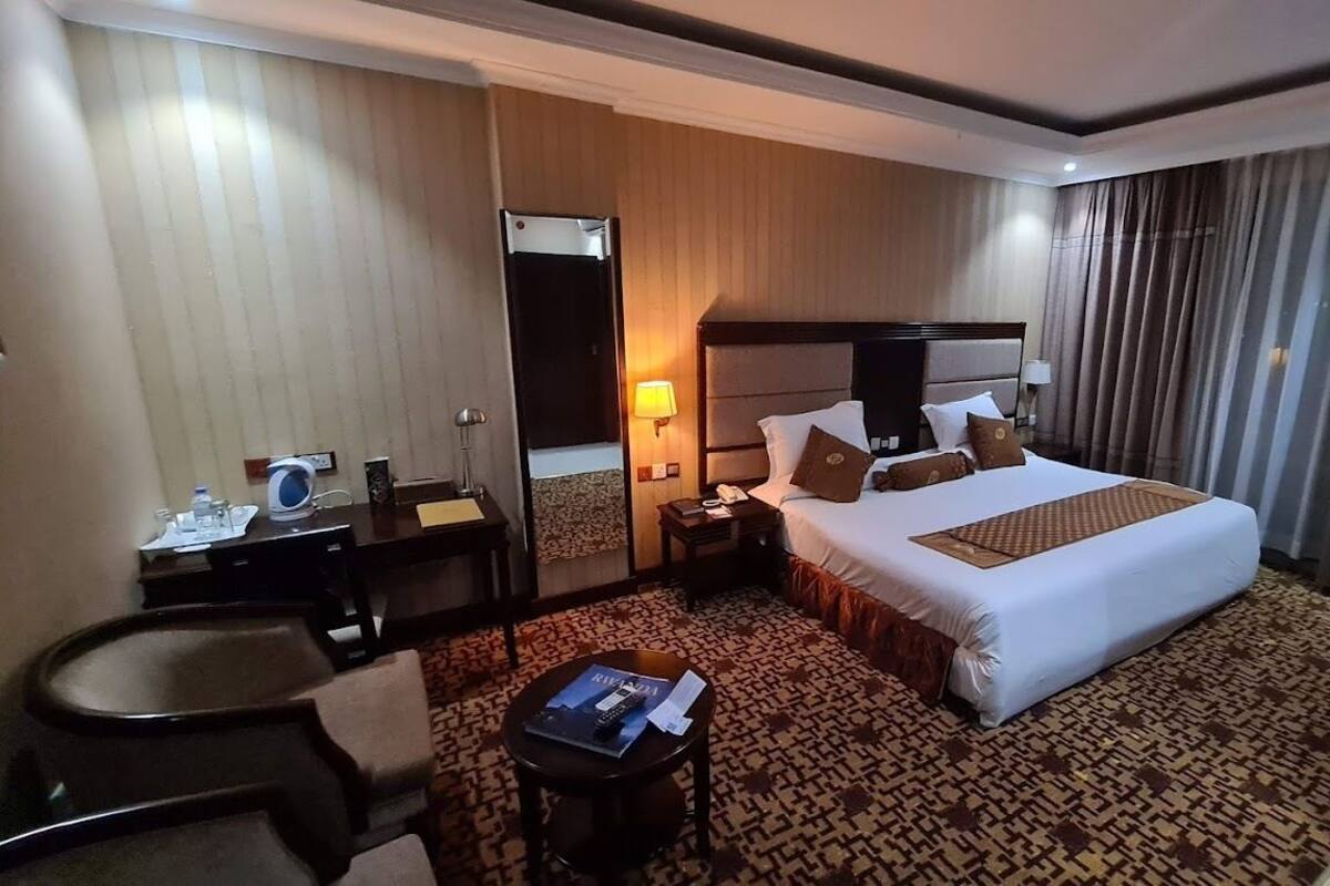 A hotel room with a large bed, a desk, a chair, and a small table with a magazine and remote control.