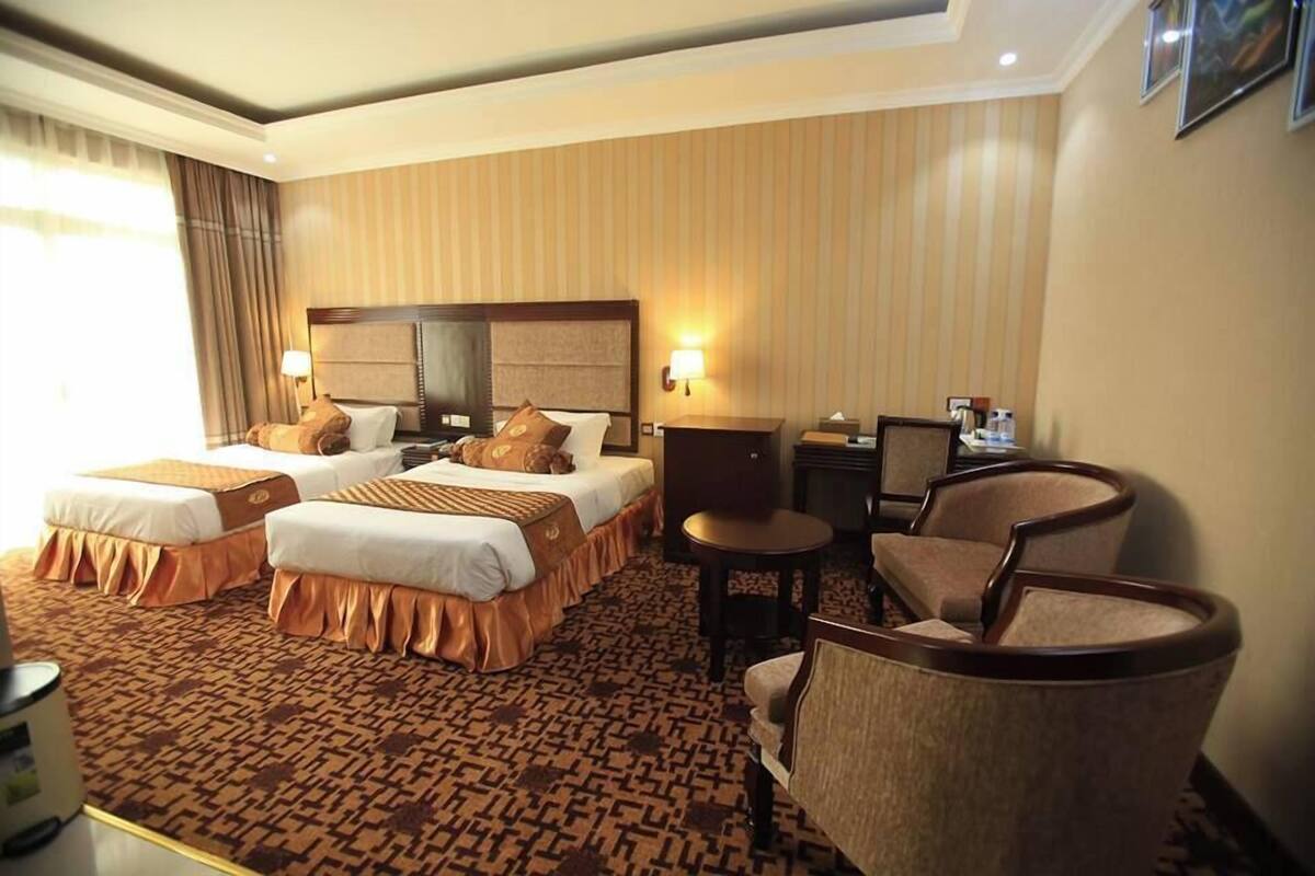A hotel room with two beds, a small table, a chair, and a desk with a lamp.