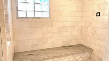 Shower area features a herringbone-patterned floor and a tiled wall, with a window for natural light and a partial wall with a textured pattern.