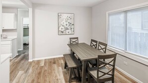 Un comedor con una mesa y sillas de madera, un cuadro en la pared y una ventana con persianas.