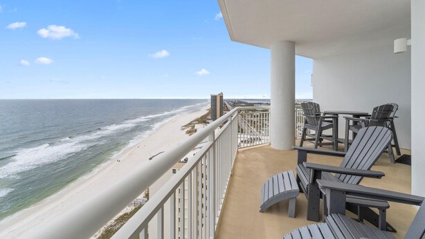 Un balcon offrant une vue sur la plage et l’océan, aménagé avec des fauteuils Adirondack et une table.