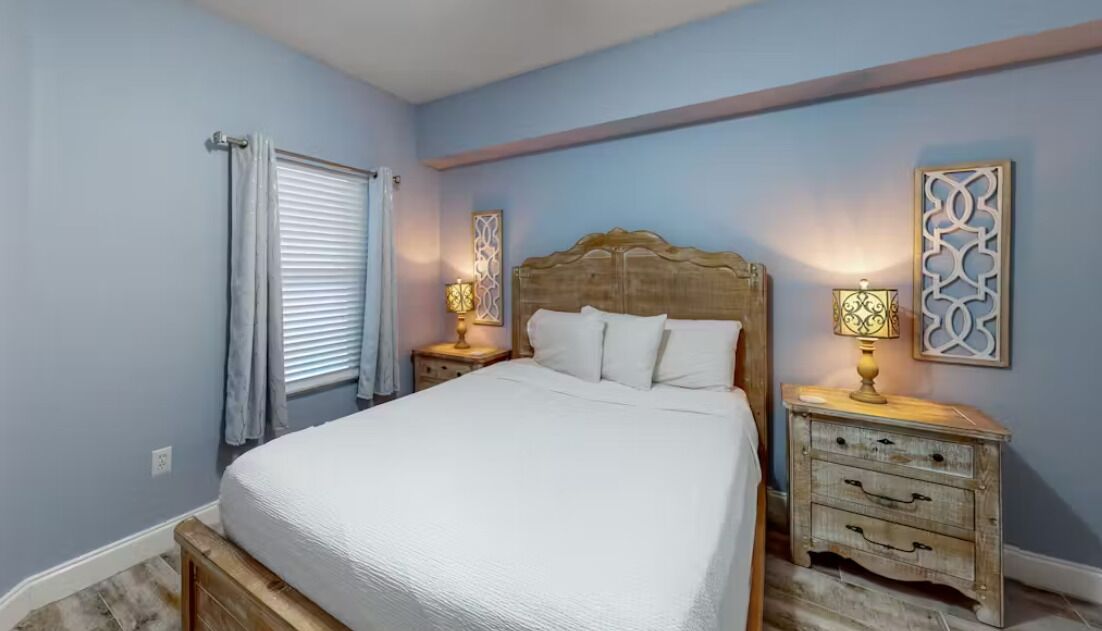 A bedroom with a wooden bed, two bedside tables with lamps, and decorative wall art.