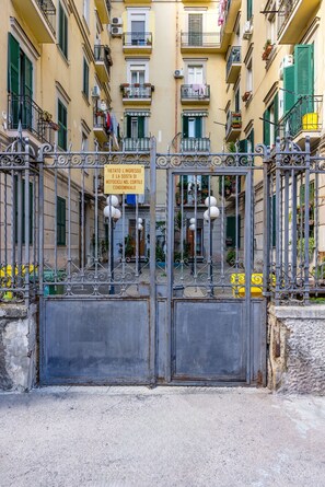 Una entrada protegida por un portón a un edificio con balcones, un letrero que indica que no se permite el acceso a motocicletas y un portón de metal con detalles decorativos.