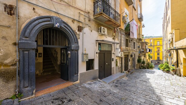 A narrow cobblestone street with a building entrance featuring a black archway and a door. - Marcellino Comfort House by Napoliapartments (Naples)