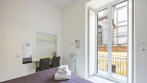 A bedroom with a bed, a desk, and a chair. There is a balcony with a view of a building. - Marcellino Comfort House by Napoliapartments (Naples)