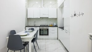 A modern kitchen with white cabinets, a stove, and a dining table with chairs. - Marcellino Comfort House by Napoliapartments (Naples)