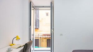 A bedroom with a bed, a desk with a chair, a yellow desk lamp, and an open door leading to a balcony. - Marcellino Comfort House by Napoliapartments (Naples)