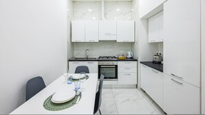 A modern kitchen with white cabinets, a gas stove, and a dining table set for two. - Marcellino Comfort House by Napoliapartments (Naples)