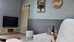Ett modernt vardagsrum med en platt-TV, en vit soffa, ett träbord, en vit pall och ett set vinglas som står på ett brickbord.