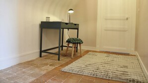 Ett rum med ett skrivbord, en pall, en lampa och en mönstrad matta på ett klinkergolv.