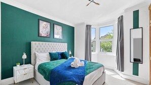 A bedroom with a large bed, a nightstand, a window with curtains, and a framed picture on the wall.