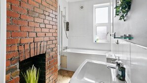 A bathroom with a brick fireplace, a bathtub, and a sink.