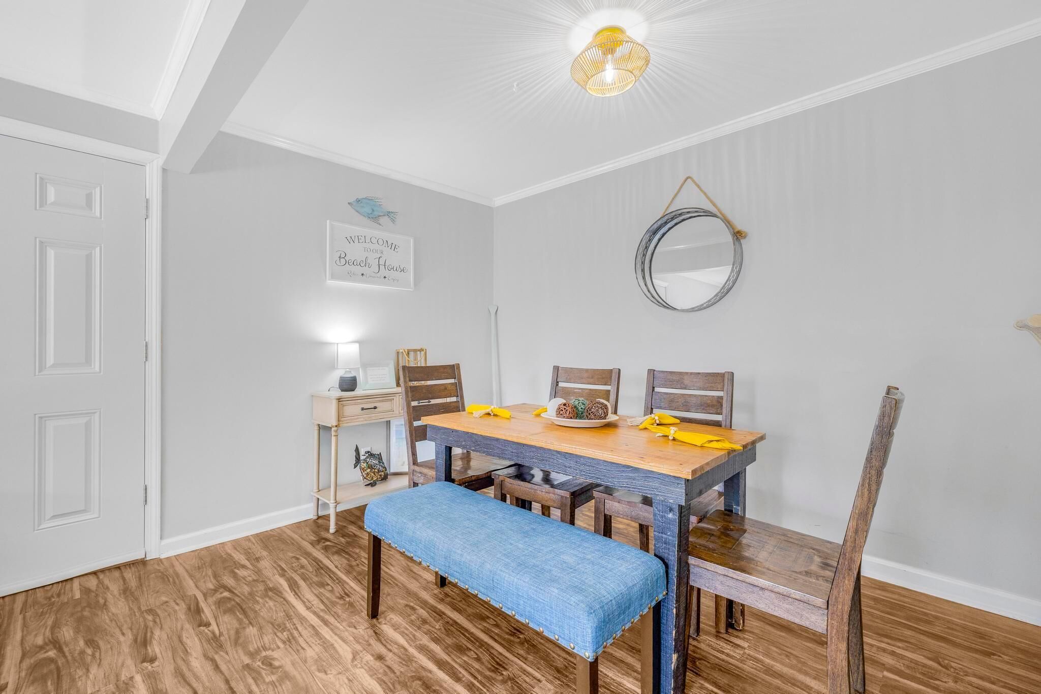 Un coin repas avec une table et des bancs en bois, une porte blanche et un miroir fixé au mur.
