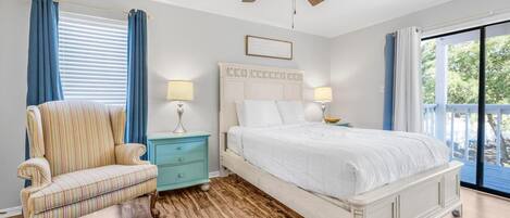 A bedroom with a bed, a chair, a nightstand, a ceiling fan, and a view of the outdoors.