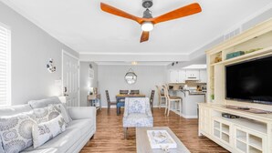 A modern living room with a sofa, coffee table, TV, and ceiling fan. - Romar Village 112 (Orange Beach)