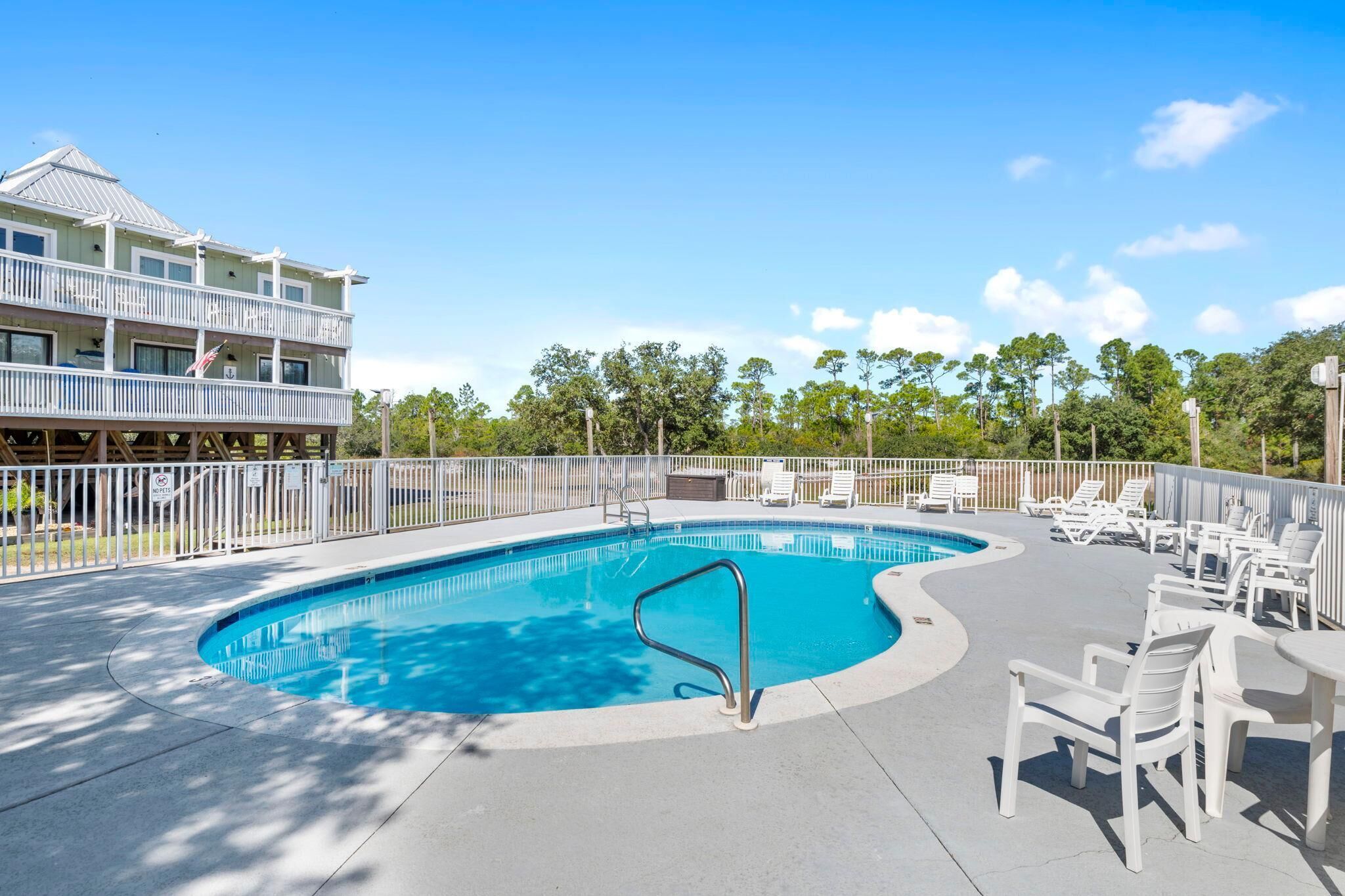 A swimming pool with a curved edge, surrounded by white lounge chairs and a white fence.