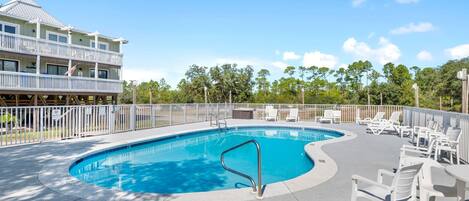 A swimming pool with a curved edge, surrounded by white lounge chairs and a white fence.