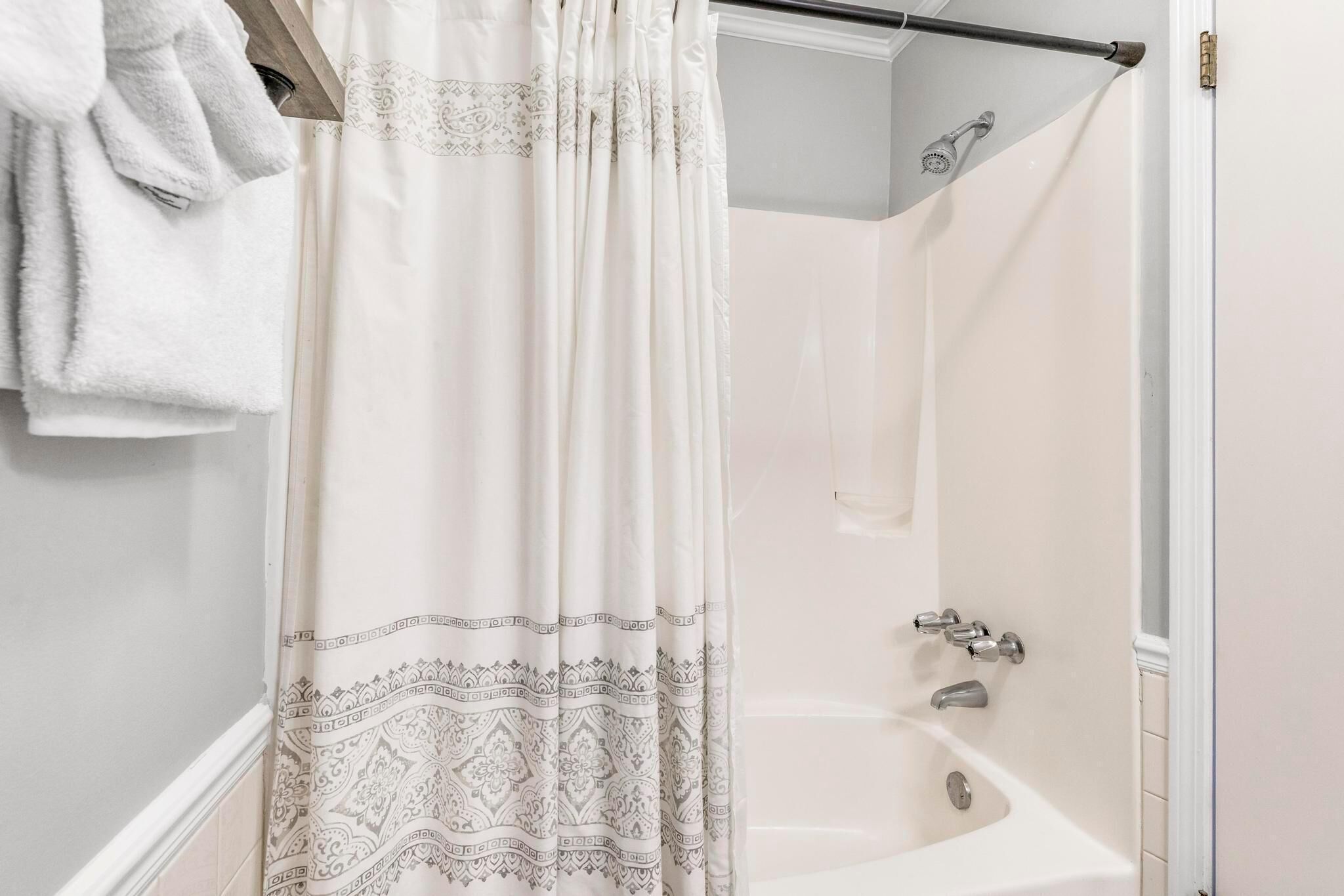 A bathroom with a shower curtain, a bathtub, and a towel rack with towels.