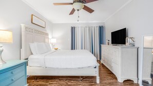 A bedroom with a bed, a ceiling fan, a dresser, a television, and curtains. - Romar Village 112 (Orange Beach)