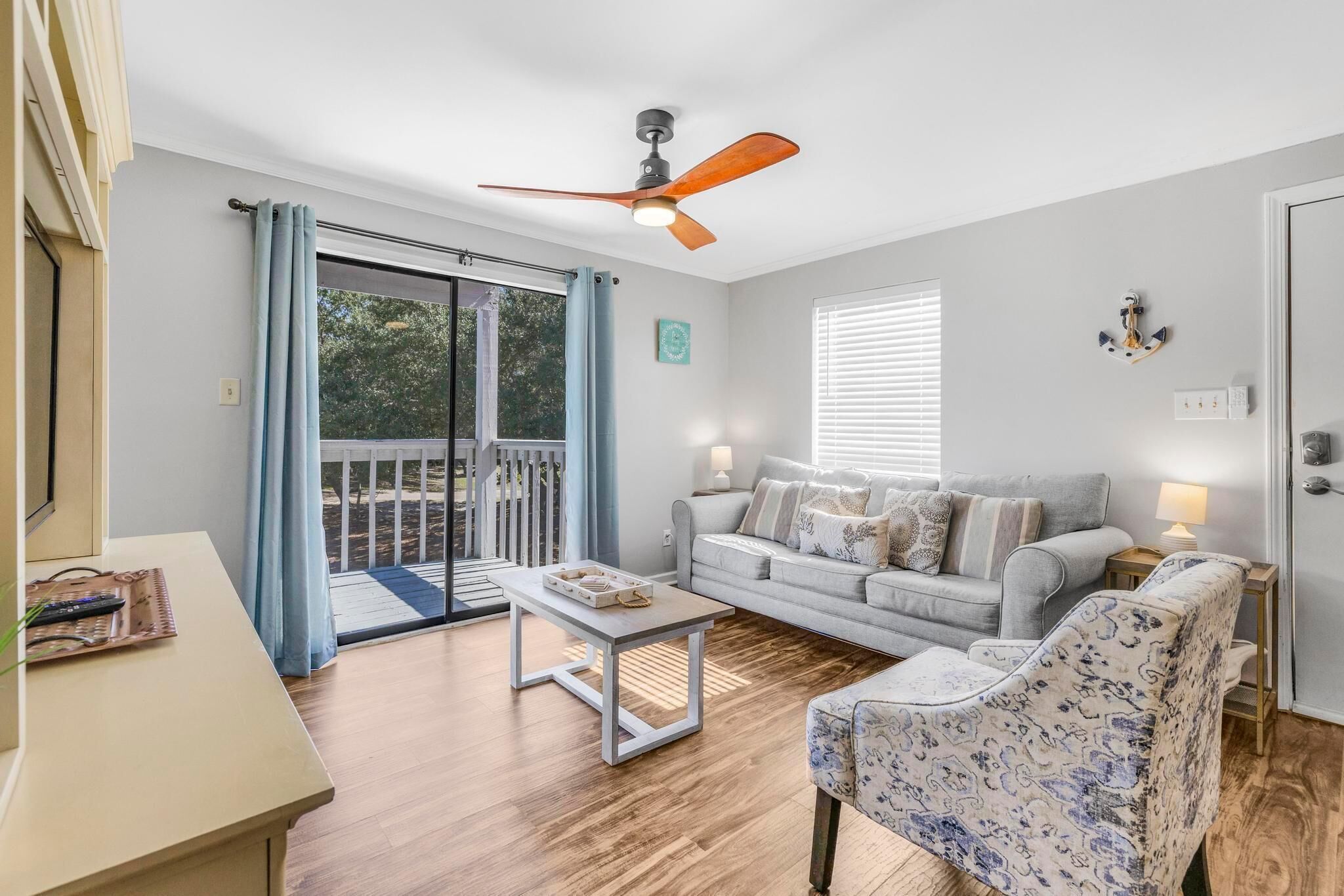 A living room with a sofa, armchair, and coffee table, a ceiling fan, and a sliding glass door leading to an outdoor area.