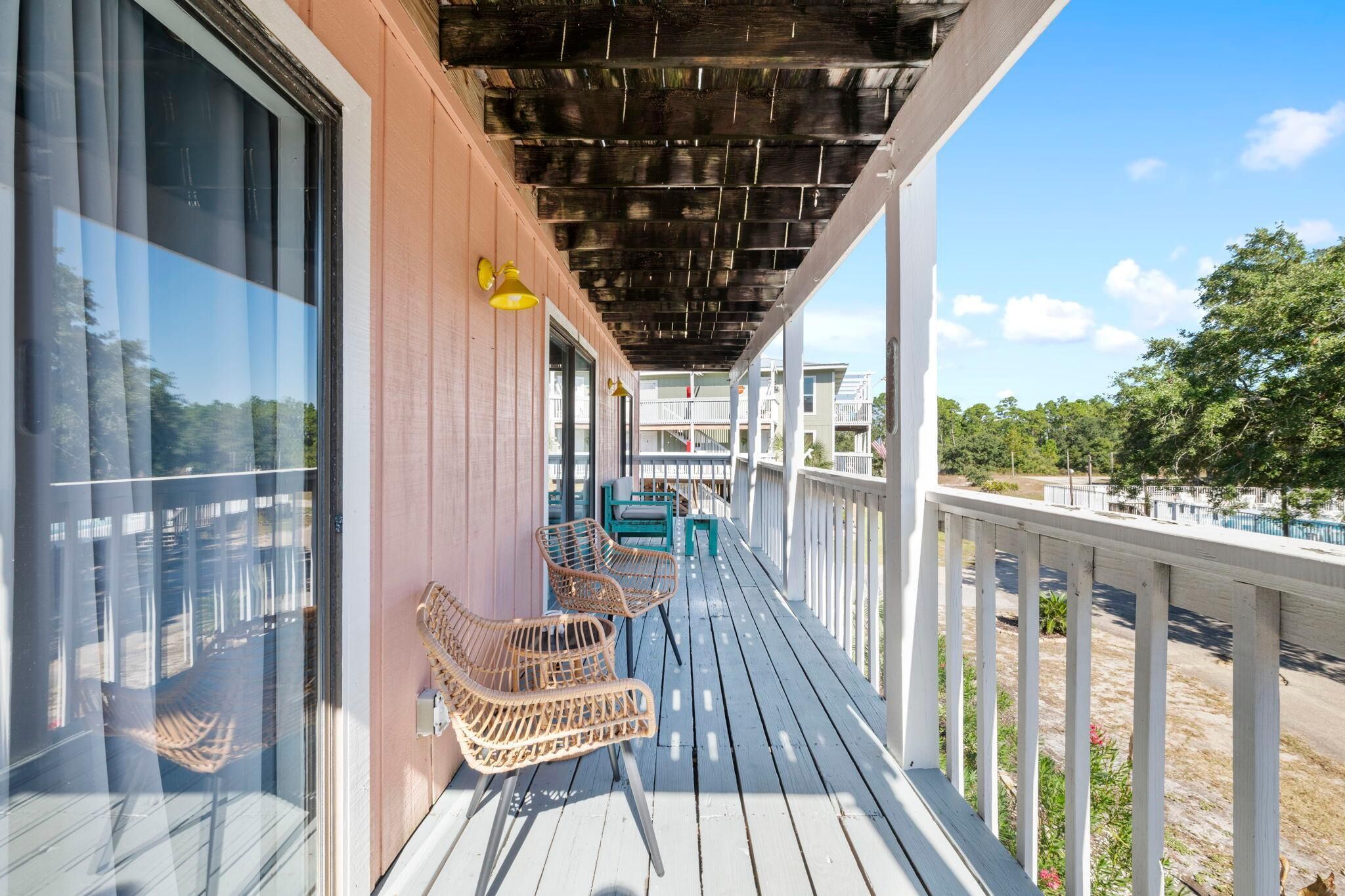 A wooden deck with wicker chairs and a table, overlooking a body of water and a residential area.