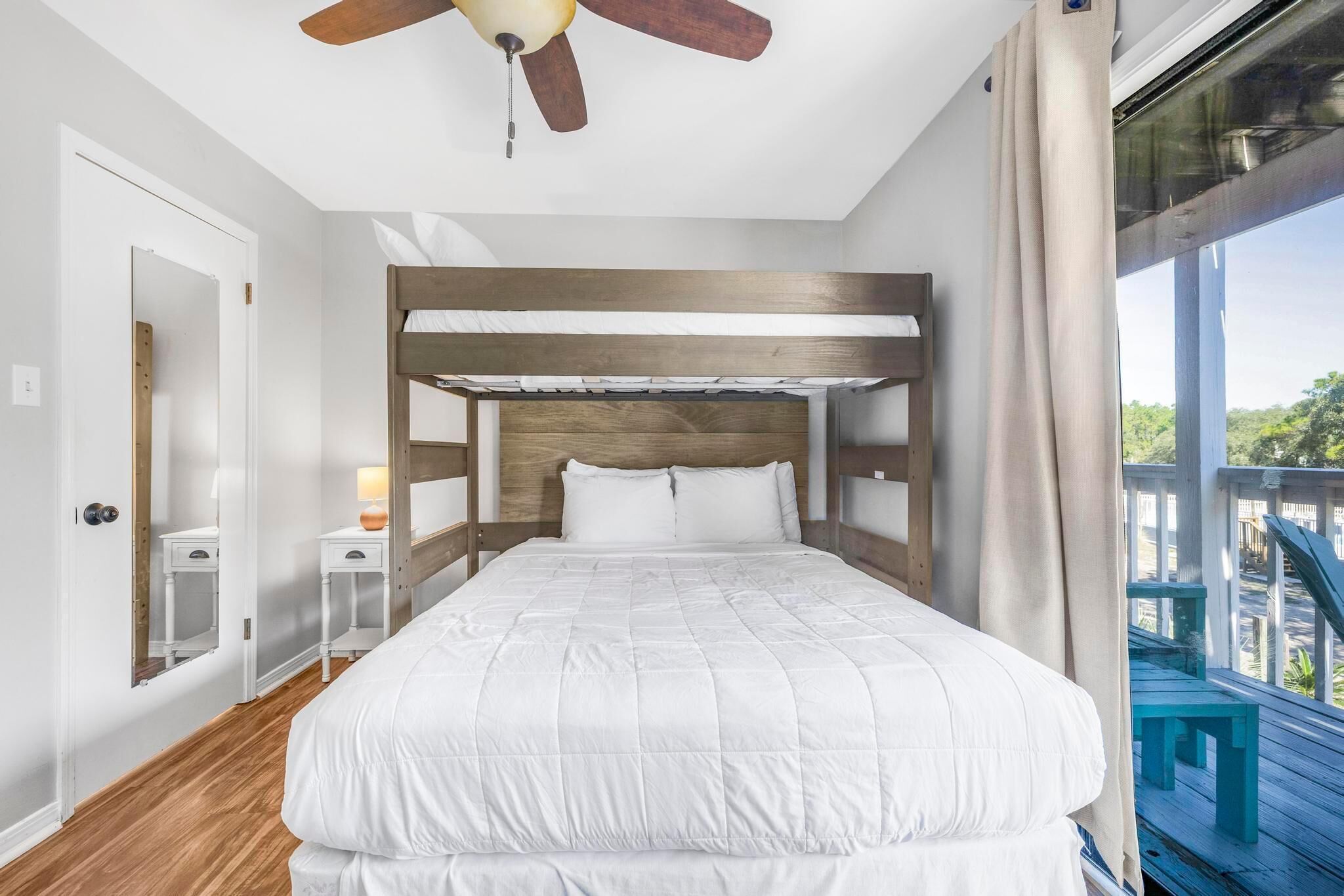 A bedroom with a bunk bed, a ceiling fan, a window with curtains, and a view of the outdoors.