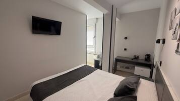 Un dormitorio moderno con cama, televisor, escritorio y espejo.