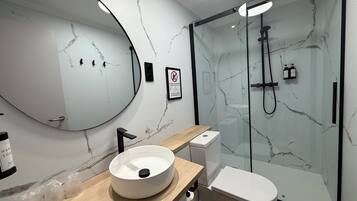 Ein modernes Badezimmer mit Marmorwand, einem runden Waschbecken, einer Toilette und einer Duschkabine.