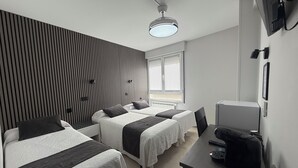 Ein modernes Hotelzimmer mit zwei Betten, einem Schreibtisch, einem Computer und einem Fenster mit Jalousien.