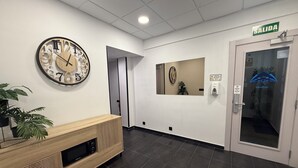 Ein Empfangsbereich mit einer Holztischplatte, einer großen Wanduhr, einer Tür mit der Aufschrift 'SALIDA' und einer kleinen Pflanze.